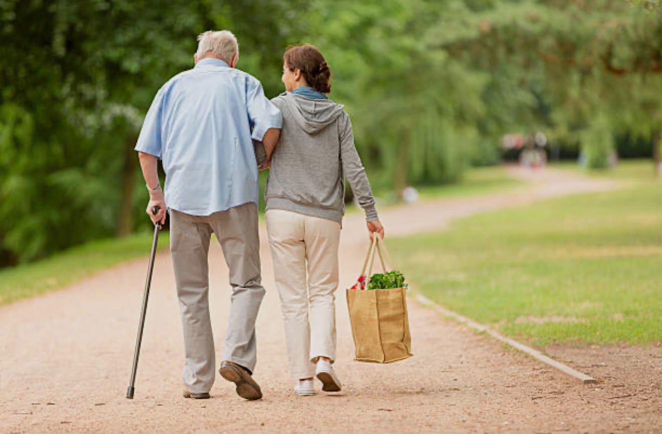 A carer walking outdoors with an older man